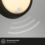 Nahaufnahme einer runden, schwarzen Akku-Außenwandleuchte mit Bewegungsmelder, montiert an einer Wand.