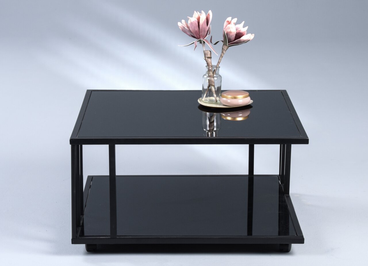 Moderne salontafel met een zwart glazen blad en een metalen frame, versierd met een vaas en een kaars, gezien van voren.