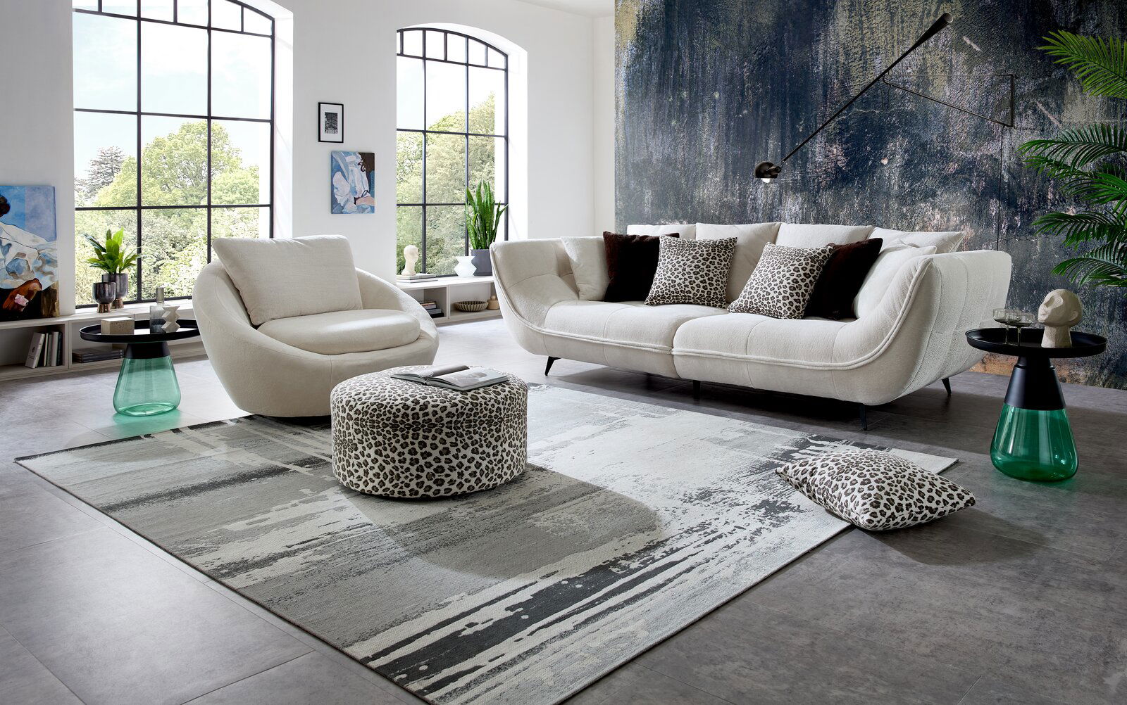 Stylife Couchtisch AMALYA Modernes Wohnzimmer mit cremefarbenem Sofa und passendem Sessel, Leopardmuster-Pouf und Kissen auf großem grauen Teppich, seitliche Perspektive auf die Sitzgruppe vor großen Fenstern und Akzentwand.