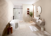 Modernes Badezimmer mit freistehender Badewanne, eleganter Waschtisch mit rundem Spiegel und mehreren Badteppichen auf dem Boden. Perspektive von der Tür aus.