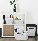 Weiße, schmale Aufbewahrungsboxen mit perforiertem Design, gefüllt mit Büchern und Garn, in einem modernen Regal von vorne betrachtet.