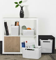 Weiße, schmale Aufbewahrungsboxen mit perforiertem Design, gefüllt mit Büchern und Garn, in einem modernen Regal von vorne betrachtet.