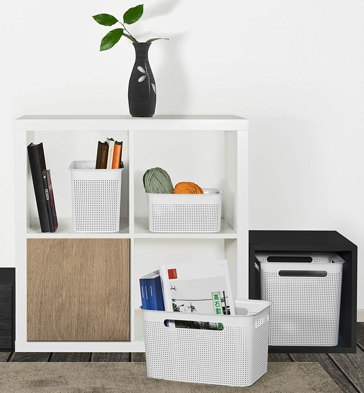 Weiße, schmale Aufbewahrungsboxen mit perforiertem Design, gefüllt mit Büchern und Garn, in einem modernen Regal von vorne betrachtet.