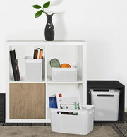 Weiße, schmale Aufbewahrungsboxen mit perforiertem Design, gefüllt mit Büchern und Garn, in einem modernen Regal von vorne betrachtet.