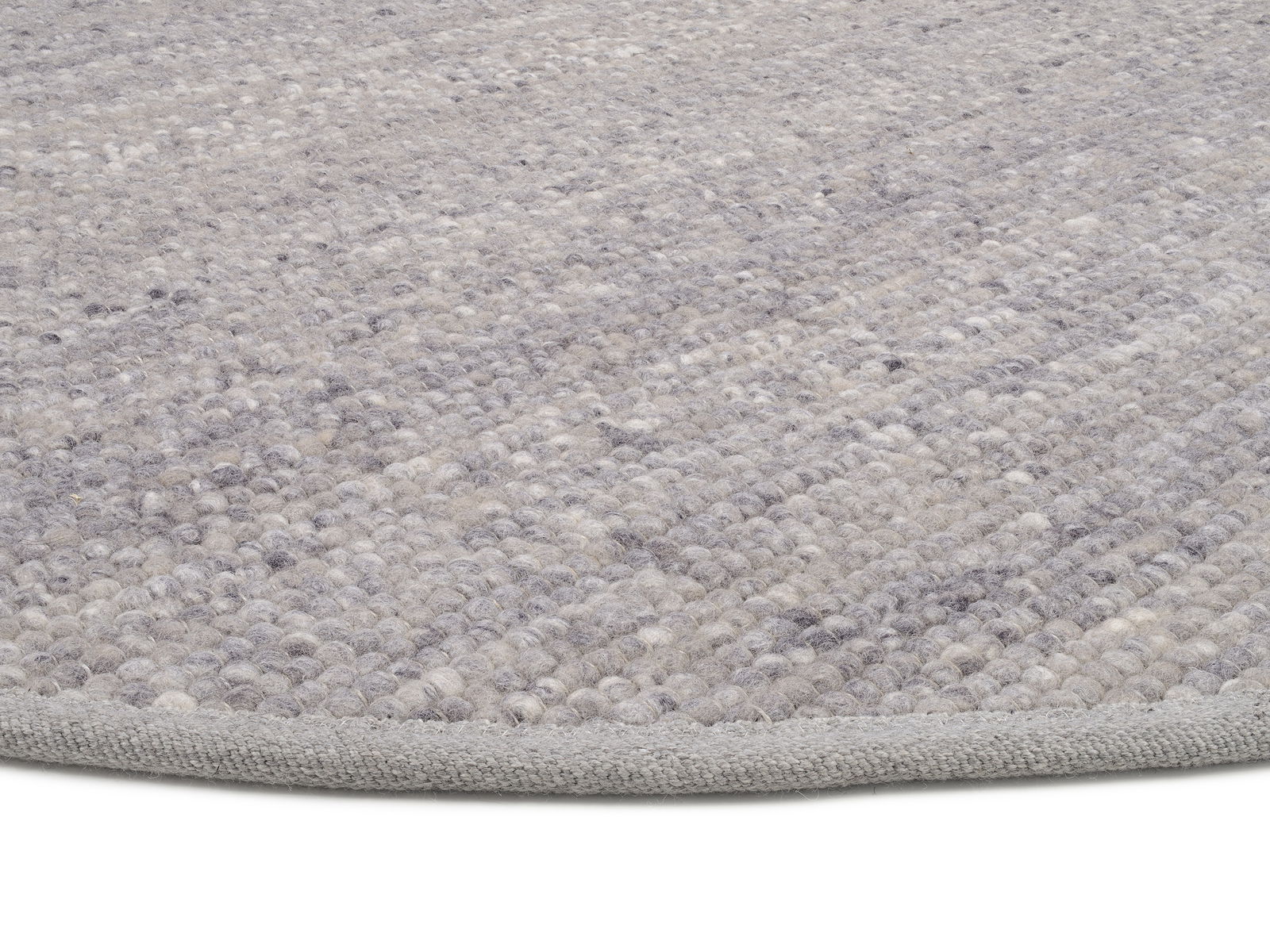 Nahaufnahme eines handgewebten Teppichs in Grautönen, von der Seite fotografiert.