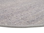 Nahaufnahme eines handgewebten Teppichs in Grautönen, von der Seite fotografiert.