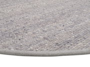 Nahaufnahme eines handgewebten Teppichs in Grautönen, von der Seite fotografiert.