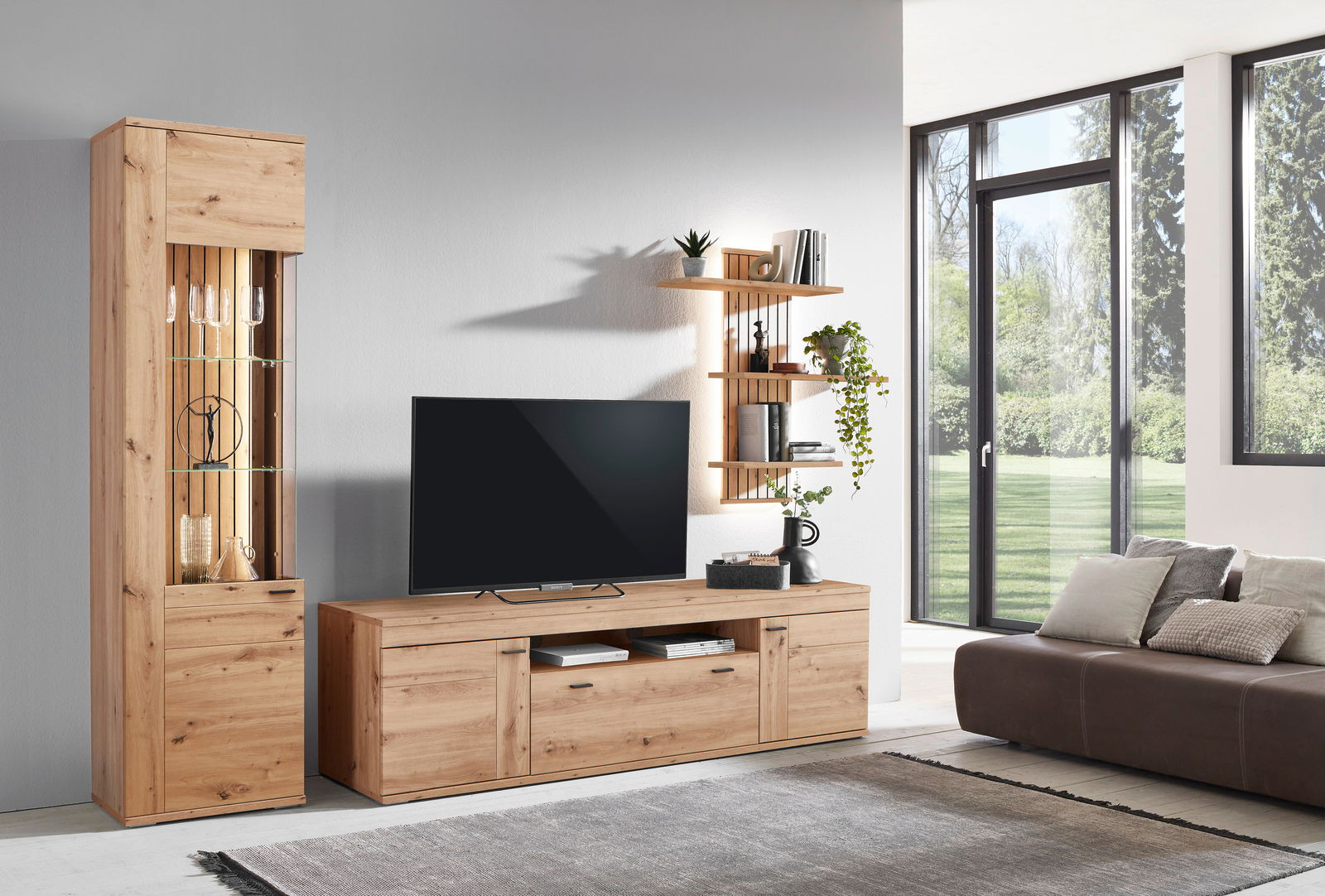 Moderne Wandkombination aus Holz mit TV-Schrank, Vitrine und Wandregalen in einem hellen Wohnzimmer, seitliche Perspektive.