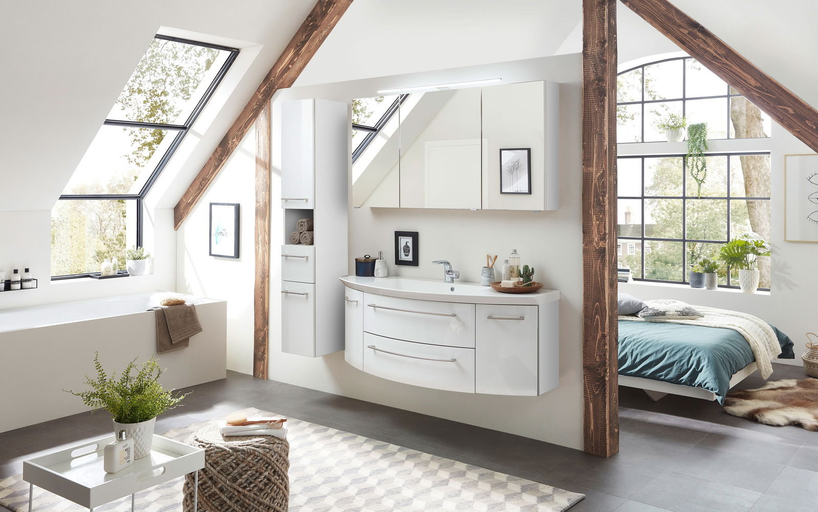 Sadena Badkombination 3-tlg. PLAKA Moderne Badkombination in einem hellen Dachgeschossbad mit großen Fenstern, bestehend aus einem weißen Waschtisch mit zwei Schubladen, einem hohen Schrank und einem Spiegelschrank. Perspektive von schräg vorne.