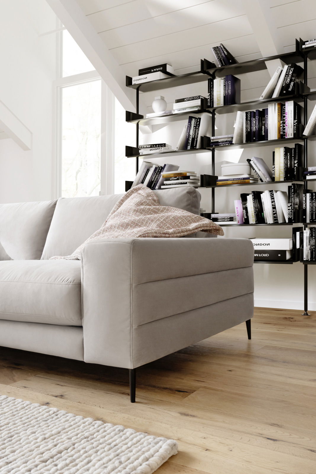 Graues Longchair-Sofa in einem modernen Wohnzimmer, seitliche Perspektive, mit Bücherregal im Hintergrund.