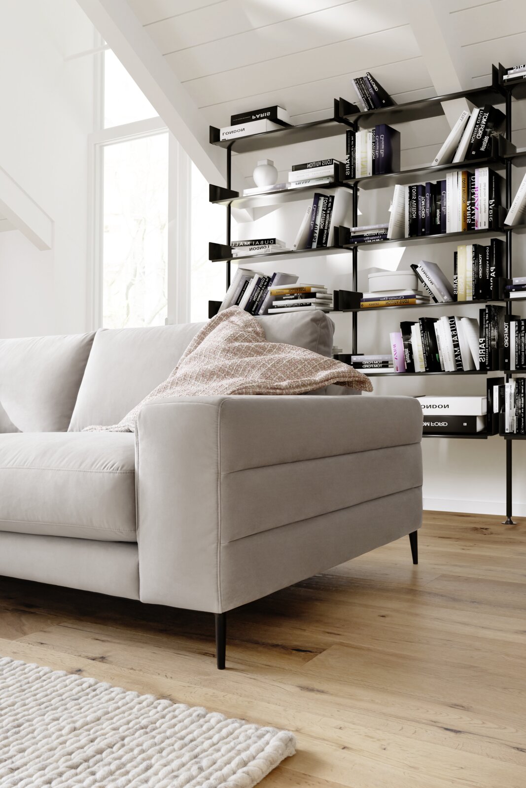Graues Longchair-Sofa in einem modernen Wohnzimmer, seitliche Perspektive, mit Bücherregal im Hintergrund.