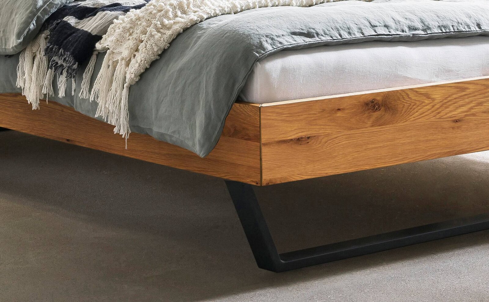 Nahaufnahme eines modernen Bettgestells aus Holz mit schwarzem Metallfuß, seitliche Perspektive.