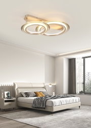 Moderne LED-Deckenleuchte mit zwei ineinander verschlungenen Ringen, von unten betrachtet, in einem stilvollen Schlafzimmer montiert.