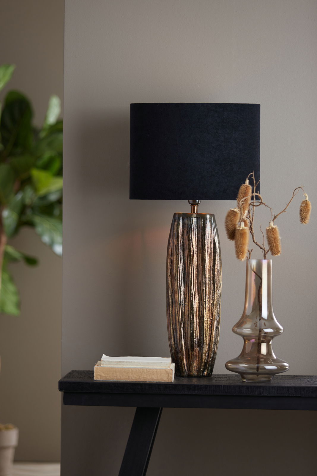 Elegante Tischlampe mit schwarzem, ovalem Lampenschirm und strukturiertem, metallisch glänzendem Fuß, seitliche Perspektive.