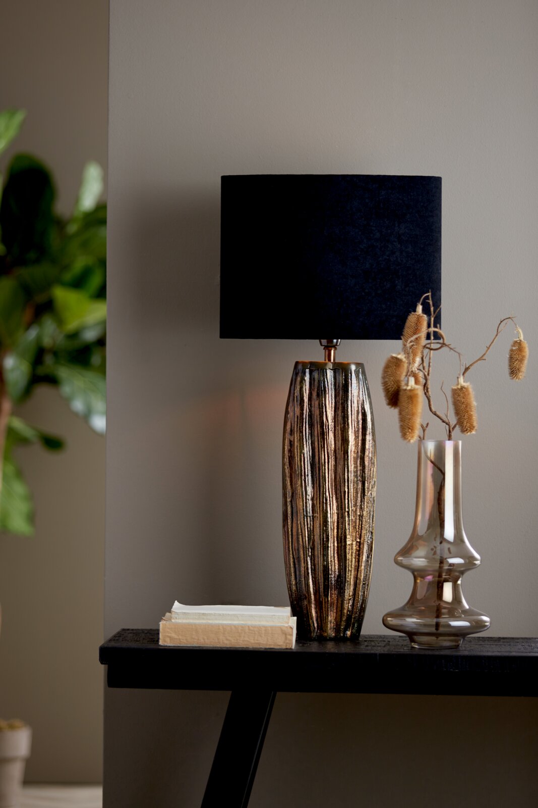 Elegante Tischlampe mit schwarzem, ovalem Lampenschirm und strukturiertem, metallisch glänzendem Fuß, seitliche Perspektive.