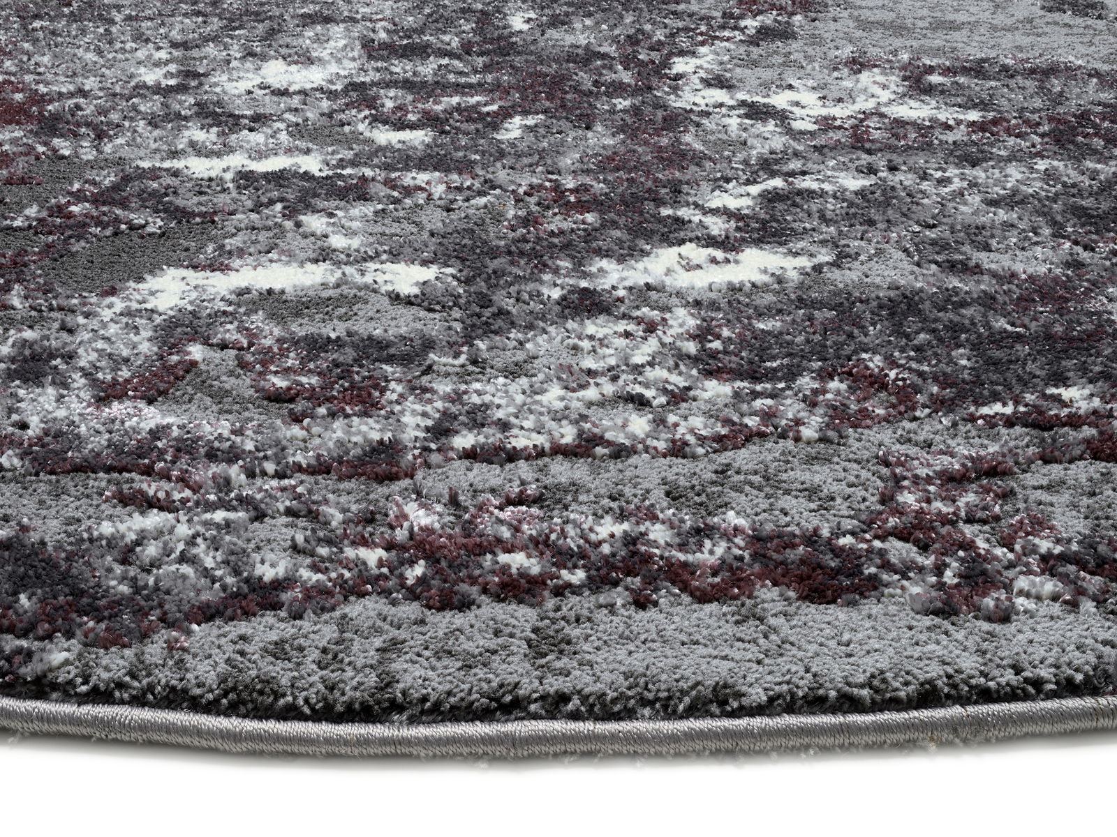 Nahaufnahme eines Designer-Teppichs mit abstraktem Muster in Grau- und Rottönen, seitliche Perspektive.