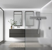 Grauer Duschabzieher aus Silikon, an einer Glasduschwand hängend, in einem modernen Badezimmer mit minimalistischer Einrichtung. Perspektive von der Seite.