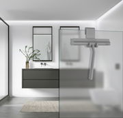 Grauer Duschabzieher aus Silikon, an einer Glasduschwand hängend, in einem modernen Badezimmer mit minimalistischer Einrichtung. Perspektive von der Seite.