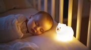 Ein schlafendes Baby neben einem leuchtenden Akku-Nachtlicht in Form eines Eisbären, seitliche Perspektive.