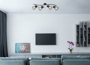 Deckenstrahler aus schwarzem Metall mit vier geometrischen Lampenschirmen, montiert an einer geschwungenen Halterung, in einem modernen Wohnzimmer von unten betrachtet.