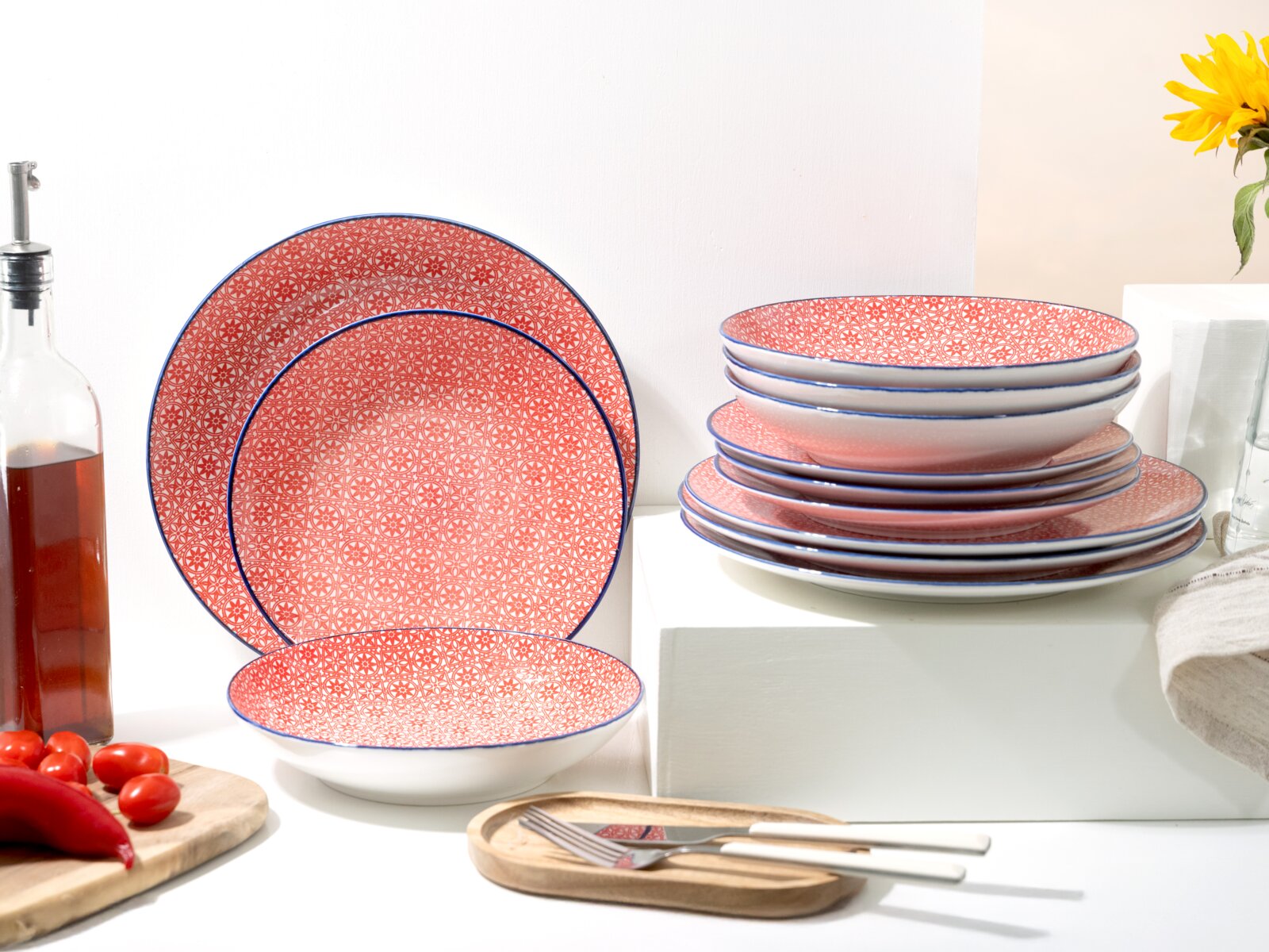 Creatable Tellerset 12-tlg MEDITERRAN Rot gemustertes Keramik-Geschirrset mit blauer Randlinie, Teller und Schalen dekorativ gestapelt und aufgestellt auf hellem Tisch, seitliche Frontansicht.