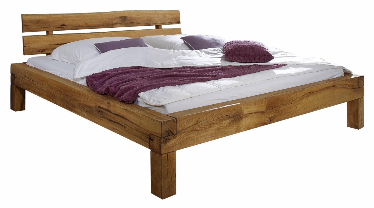 Linea Natura Balkenbett HORST Holzbalkenbett mit natürlicher Holzmaserung, seitliche Perspektive, mit weißer Bettwäsche und lila Kissen dekoriert.