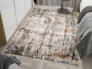 Designer Teppich mit abstraktem Muster in Grau-, Beige- und Orangetönen, auf einem Holzboden neben einem Bett und einem runden Tisch, aus der Vogelperspektive fotografiert.