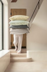 Person trägt einen Stapel gestreifter Kissenbezüge in verschiedenen Farben eine Treppe hinauf, seitliche Perspektive.