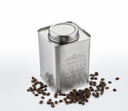 Silberne Vorratsdose für Kaffee mit Deckel, umgeben von Kaffeebohnen, aus leicht erhöhter Perspektive fotografiert.