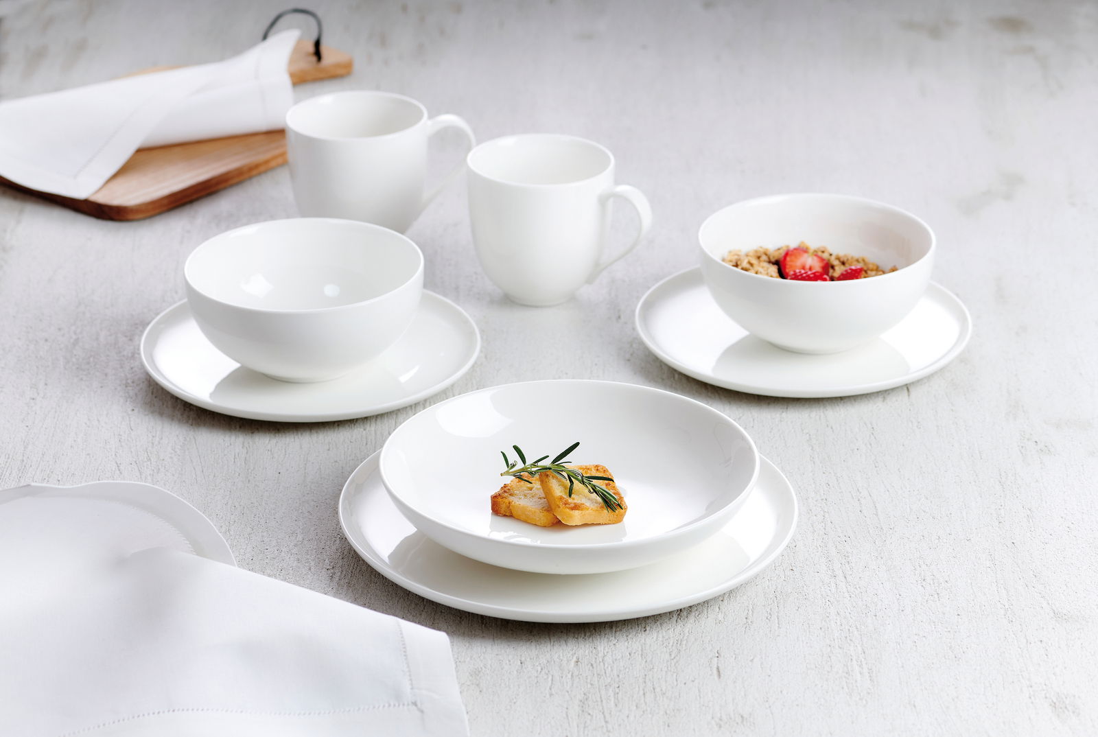 Weißes Kombiservice Skagen 30-tlg. aus Porzellan, bestehend aus Tassen, Schalen und Tellern, auf einem hellen Tisch von oben fotografiert.