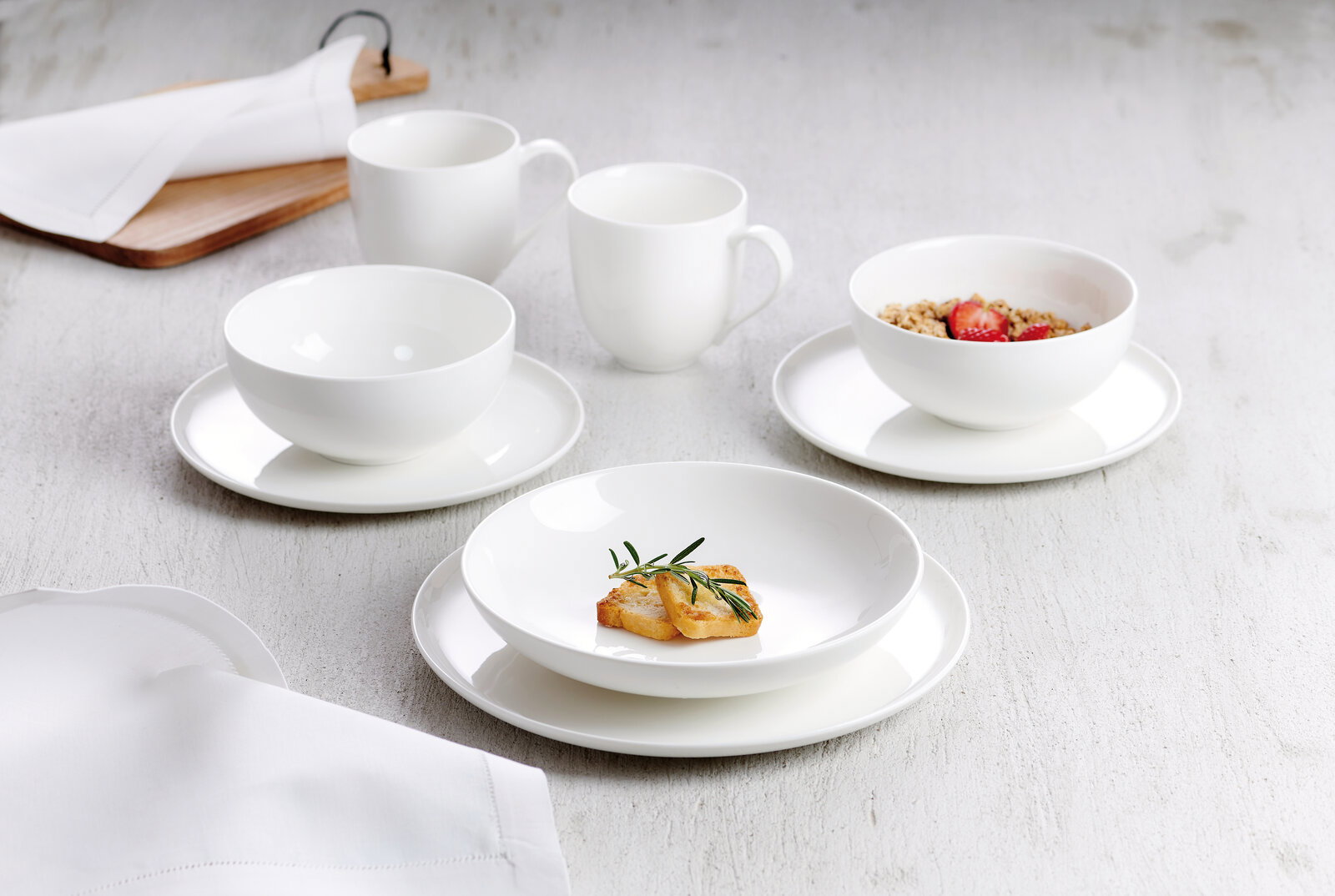 Weißes Kombiservice Skagen 30-tlg. aus Porzellan, bestehend aus Tassen, Schalen und Tellern, auf einem hellen Tisch von oben fotografiert.