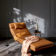 Karamellfarbene Leder-Relaxliege mit Kopfkissen und Decke in modernem Wohnraum, schräg von vorn links fotografiert