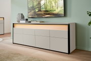 Modernes TV-Lowboard in hellem Holz mit schwarzem Rahmen, seitliche Perspektive, dekoriert mit Vasen und Büchern, unter einem an der Wand montierten Fernseher.