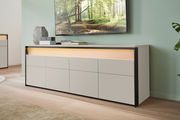 Modernes TV-Lowboard in hellem Holz mit schwarzem Rahmen, seitliche Perspektive, dekoriert mit Vasen und Büchern, unter einem an der Wand montierten Fernseher.