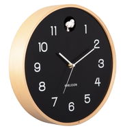 Moderne Wanduhr mit schwarzem Zifferblatt, weißen Zahlen und Zeigern, umgeben von einem hellen Holzrahmen. Perspektive von schräg vorne.