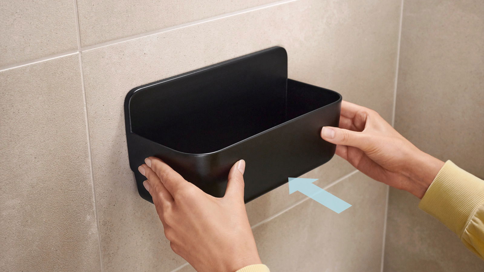 Schwarzer Duschkorb von tesa Lavaa, der an einer Badezimmerwand montiert wird. Frontalansicht.