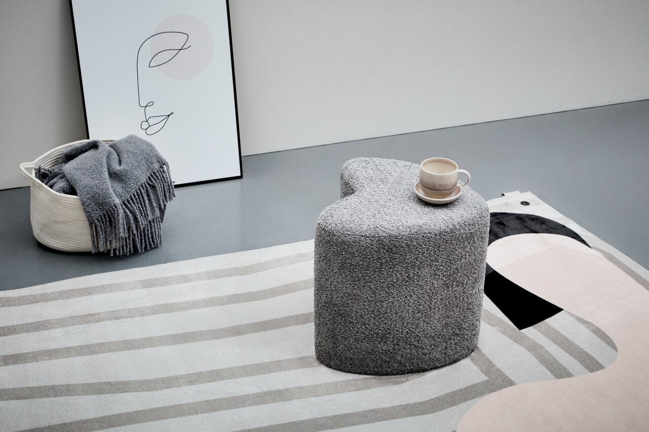 Grauer, herzförmiger Hocker XORA ANIKA in einer modernen Wohnumgebung, seitliche Perspektive, mit einer Tasse auf der Oberfläche.