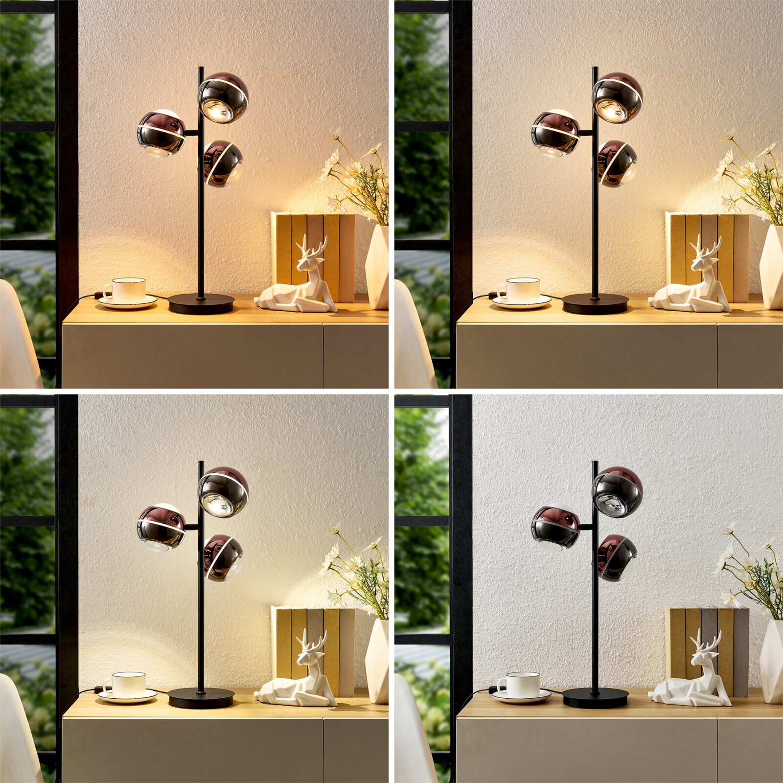 Moderne schwarze Tischlampe mit drei kugelförmigen, spiegelnden Schirmen in Roségold/Chrom auf Holz-Board, warm leuchtend neben Tasse, Büchern und Deko-Hirsch; frontale Perspektive auf dem Sideboard.
