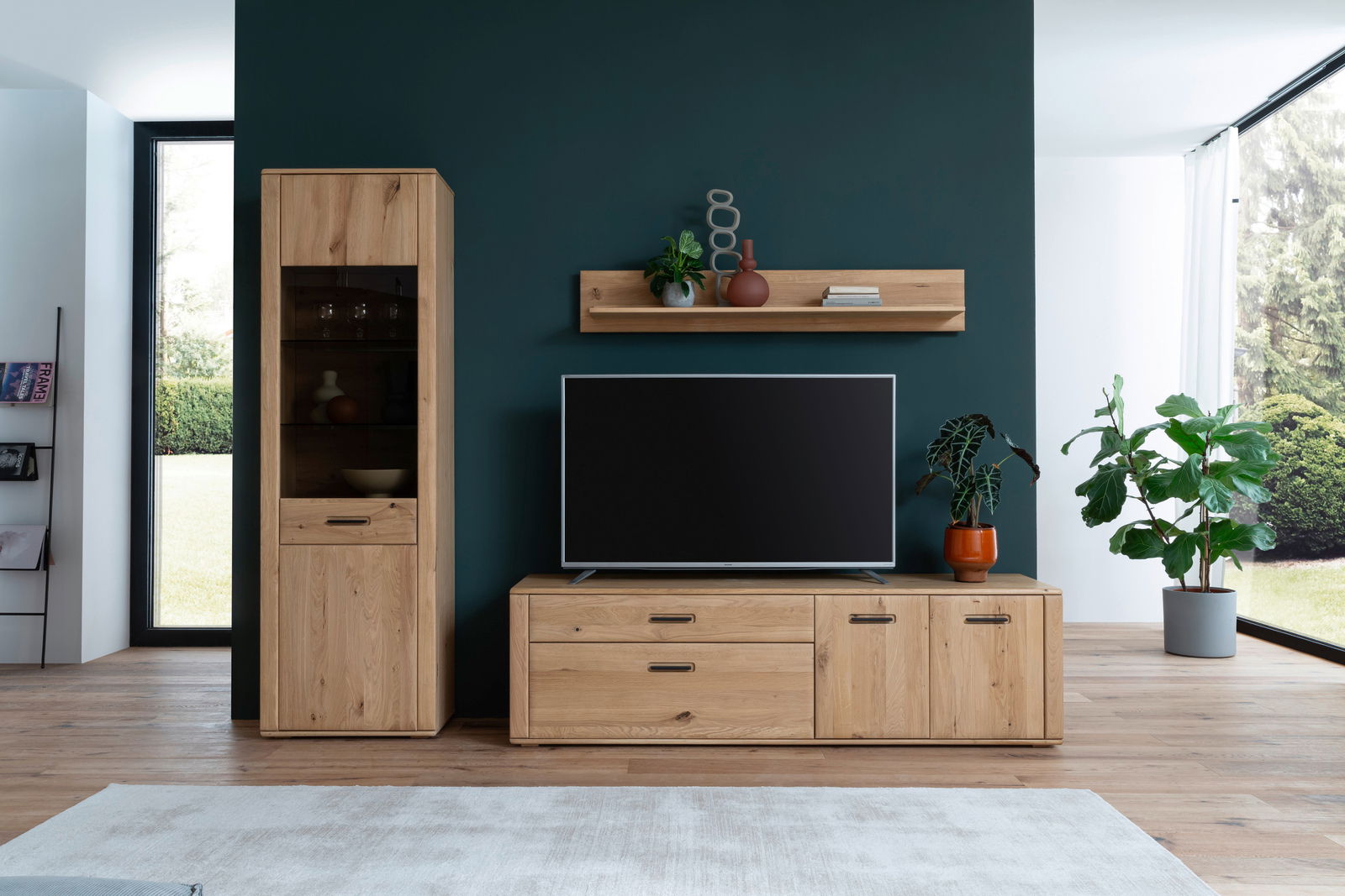 Frontale Ansicht der Cantus Wandkombination ASINARA in einem modernen Wohnzimmer mit Holzschränken, einem Fernseher und dekorativen Pflanzen.