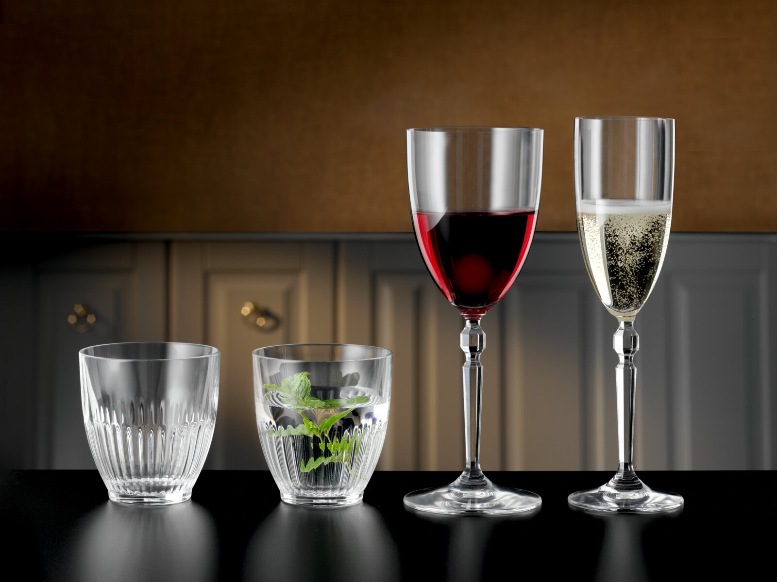 Nachtmann Weinglas 2er-Set HERITAGE Vier transparente Gläser auf schwarzer Tischplatte in Frontalansicht: zwei Tumbler (eins leer, eins mit Wasser und Minze) sowie ein Rotweinglas und ein Sektglas mit Getränken vor unscharfem Küchenhintergrund.