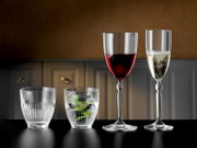 Vier transparente Gläser auf schwarzer Tischplatte in Frontalansicht: zwei Tumbler (eins leer, eins mit Wasser und Minze) sowie ein Rotweinglas und ein Sektglas mit Getränken vor unscharfem Küchenhintergrund.