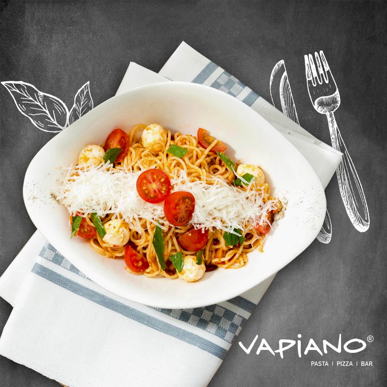 Pastaschale mit Spaghetti, Kirschtomaten, Mozzarella und geriebenem Käse, von oben fotografiert, auf einem Tisch mit Serviette und Vapiano-Logo.
