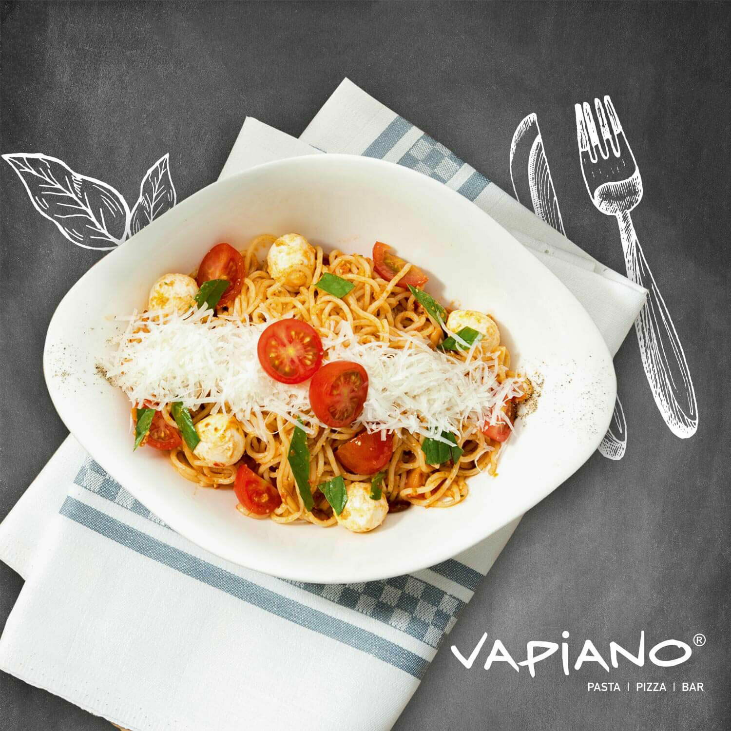 Pastaschale mit Spaghetti, Kirschtomaten, Mozzarella und geriebenem Käse, von oben fotografiert, auf einem Tisch mit Serviette und Vapiano-Logo.