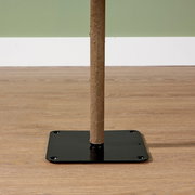 Nahaufnahme eines Holzstamms, der in einer schwarzen Metallbasis auf einem Holzboden steht, seitliche Perspektive.