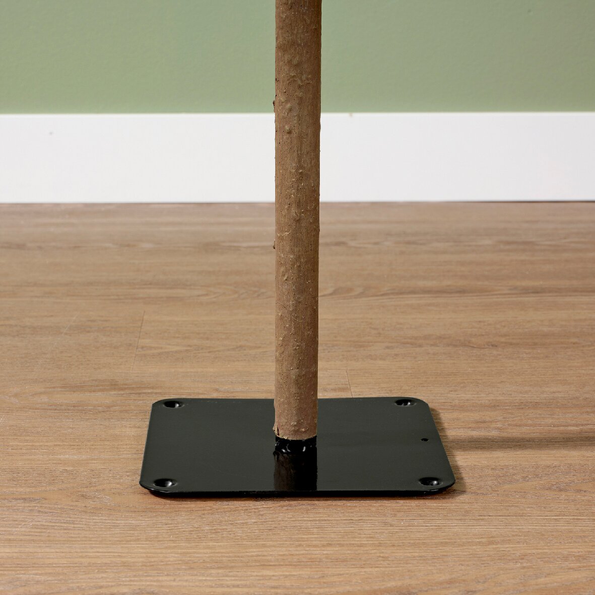 Nahaufnahme eines Holzstamms, der in einer schwarzen Metallbasis auf einem Holzboden steht, seitliche Perspektive.