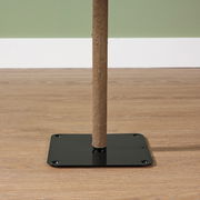 Nahaufnahme eines Holzstamms, der in einer schwarzen Metallbasis auf einem Holzboden steht, seitliche Perspektive.