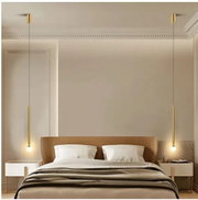 Modernes Schlafzimmer mit Doppelbett und zwei schlanken goldfarbenen Pendelleuchten neben dem Kopfteil, frontale Perspektive.