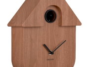 Vooraanzicht van een moderne wandklok in de vorm van een houten vogelhuisje, met zwarte wijzers en een ronde wijzerplaat.