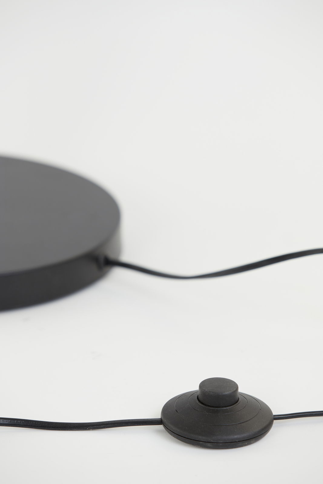 Nahaufnahme der Basis einer Stehleuchte mit einem schwarzen Fußschalter und Kabel, seitliche Perspektive.