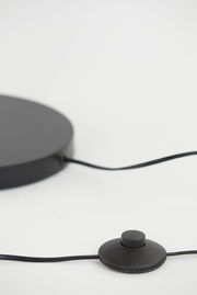 Nahaufnahme der Basis einer Stehleuchte mit einem schwarzen Fußschalter und Kabel, seitliche Perspektive.